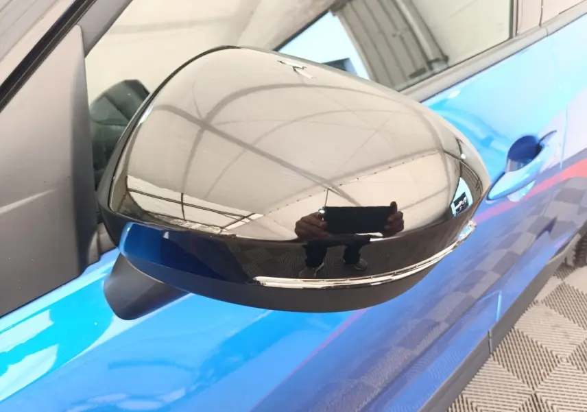 Gros plan sur le rétroviseur droit noir brillant du Nissan Juke bleu, avec poignée de porte visible en arrière-plan.