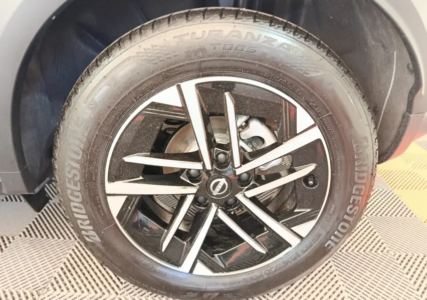 Gros plan sur la jante alliage noire et argentée du Nissan Juke bleu, mettant en valeur le logo Nissan central.