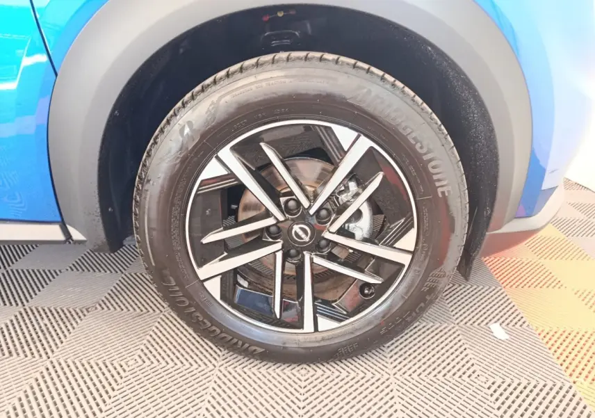 Gros plan sur la roue avant droite du Nissan Juke bleu 2025 avec jante alliage noir et argentée.