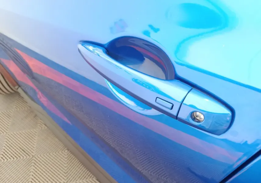 Gros plan sur la poignée de porte côté droit bleu vif du Nissan Juke DIG-T 114 BVM6 N-Connecta 2025.