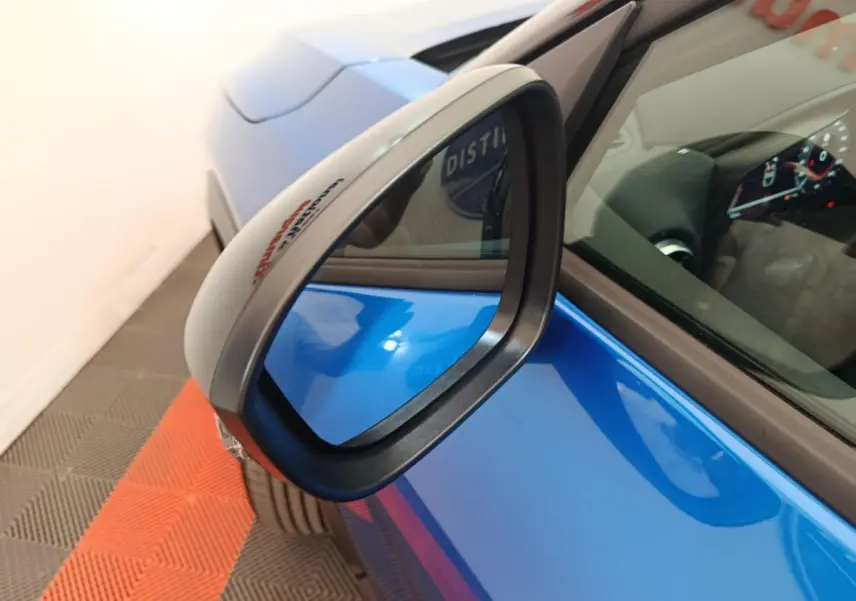 Rétroviseur côté gauche en gros plan sur Nissan Juke bleu, avec intérieur et tableau de bord partiellement visibles.