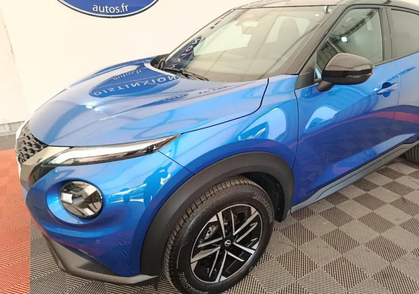 Vue 3/4 avant droit du Nissan Juke bleu 2025 avec phares ronds et jantes noires à motif argenté.