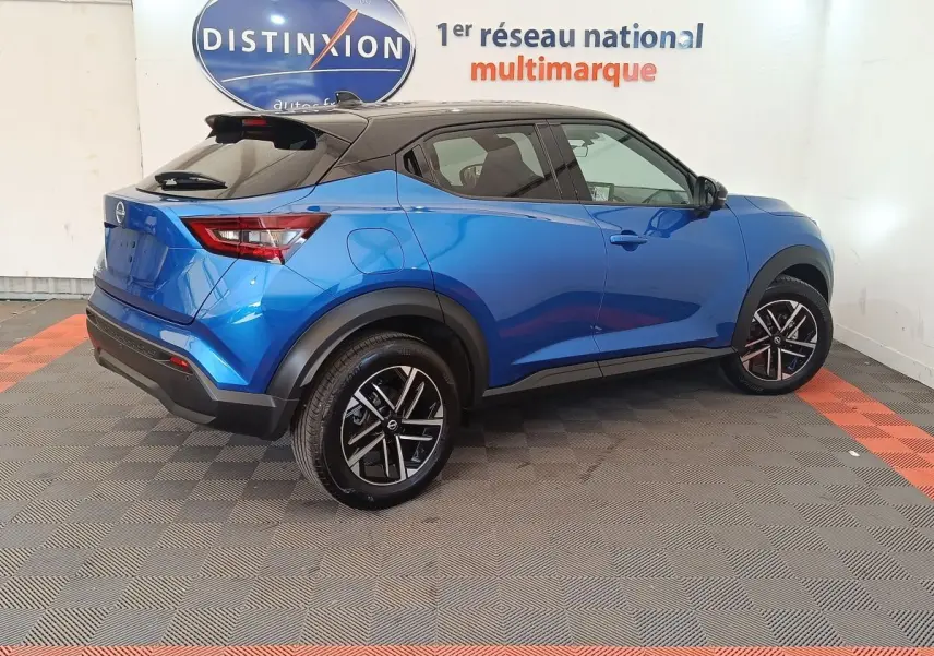 Vue 3/4 arrière droite d'un Nissan Juke bleu 2025 avec toit noir et jantes alliage bicolores.