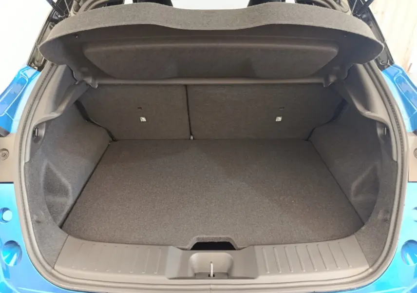 Coffre ouvert vu de l'arrière du Nissan Juke bleu 2025, espace de chargement propre et vide, banquette arrière visible.