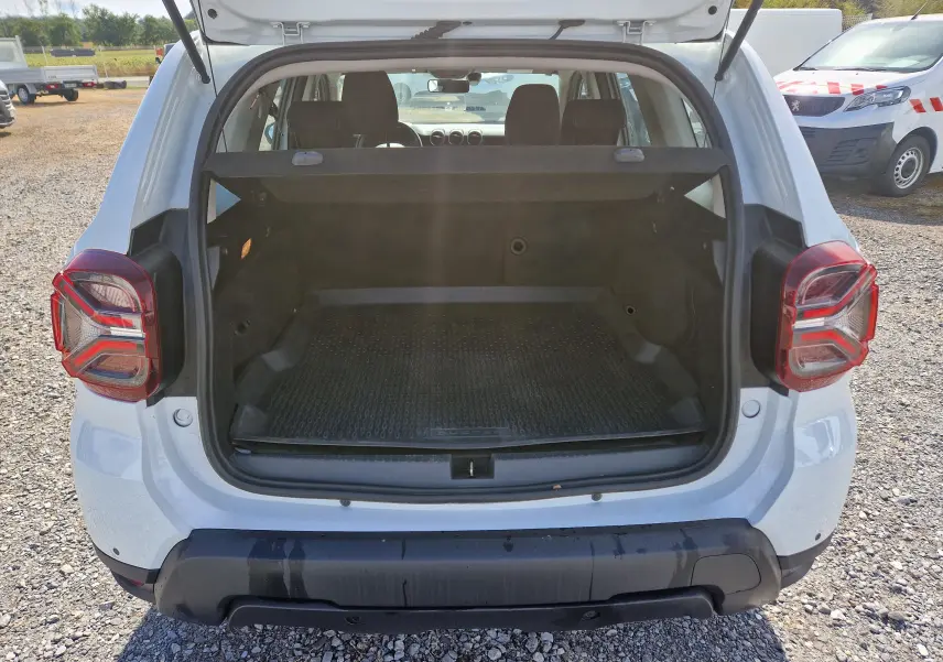 Vue arrière du coffre ouvert d'un Dacia Duster blanc 2023, montrant l'espace de chargement et les feux arrière distinctifs.