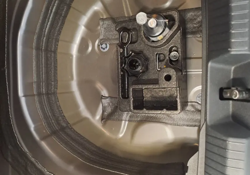 Vue rapprochée de la zone de rangement sous le coffre du Volkswagen Taigo gris cendre, montrant l'emplacement pour roue de secours.