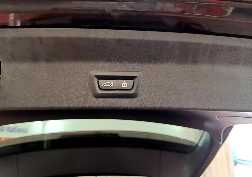 Gros plan sur le bouton de fermeture électrique du coffre du BMW X3 noir, vue depuis l'intérieur du hayon ouvert.