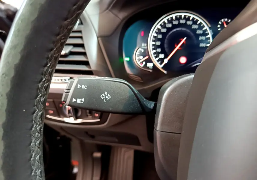 Vue rapprochée du commodo de clignotant à gauche sur le volant cuir d'un BMW X3 noir, tableau de bord éclairé.