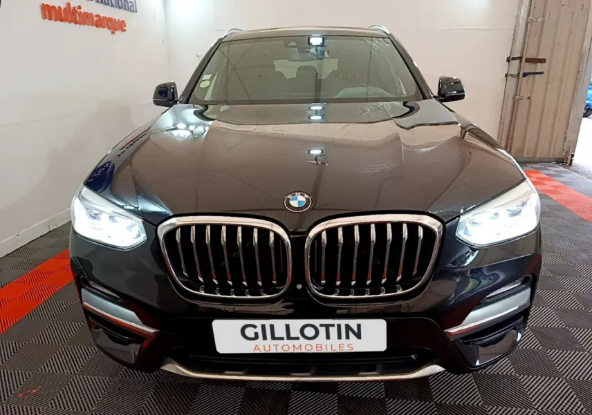 Vue frontale d'un BMW X3 noir avec phares LED allumés et calandre double haricot chromée dans un showroom.