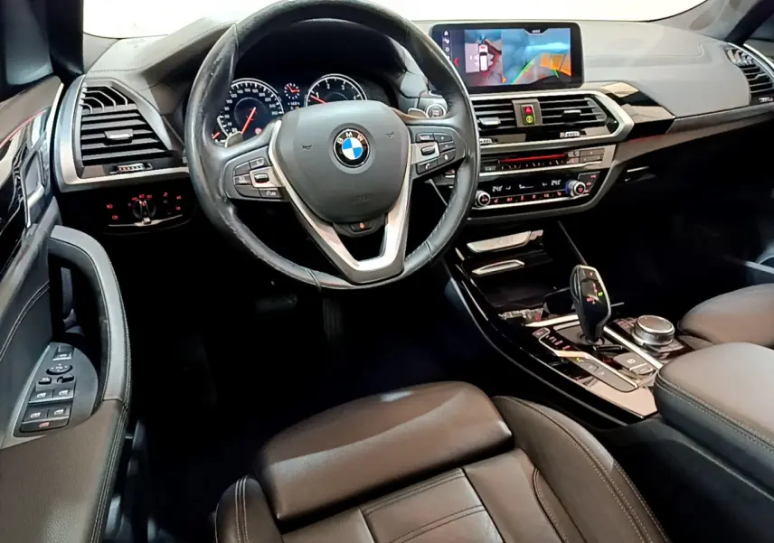 Vue intérieure côté conducteur du BMW X3 noir 2019, volant cuir, tableau de bord avec écran tactile et console centrale moderne.