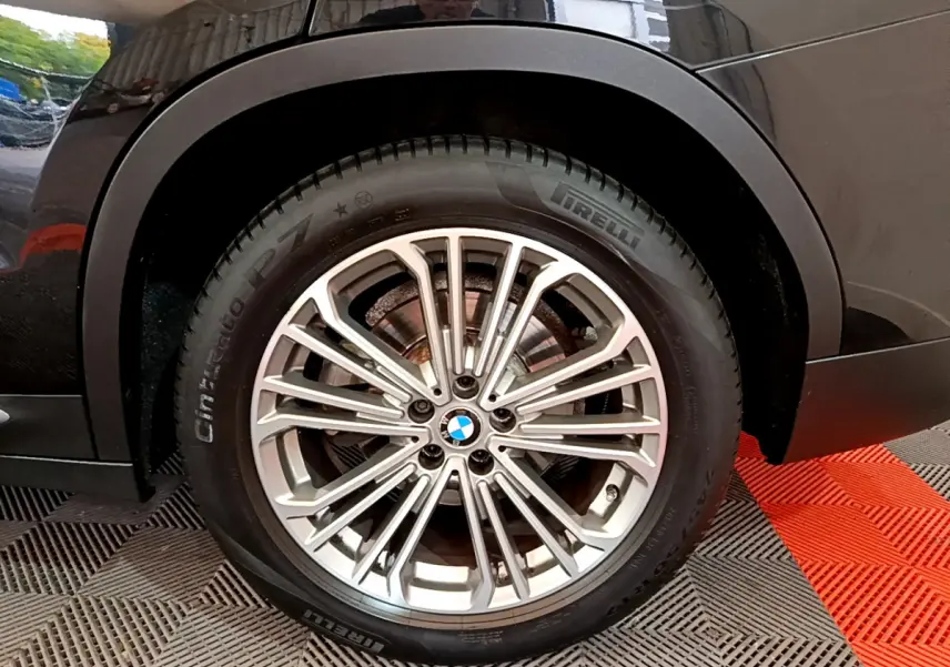 Gros plan sur la roue avant gauche du BMW X3 noir, mettant en valeur la jante alliage et le pneu Pirelli.