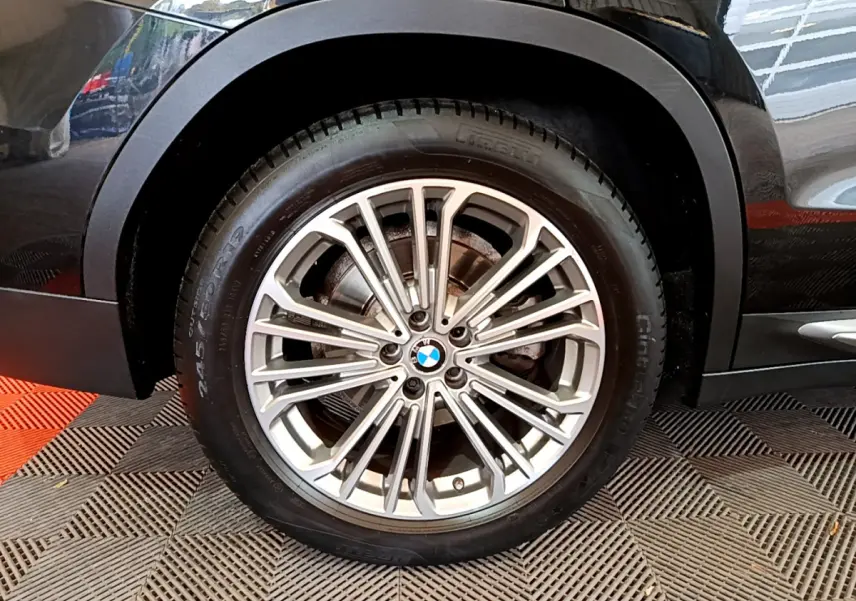 Gros plan sur la roue avant gauche du BMW X3 noir, mettant en valeur la jante alliage multi-branches et le logo central.