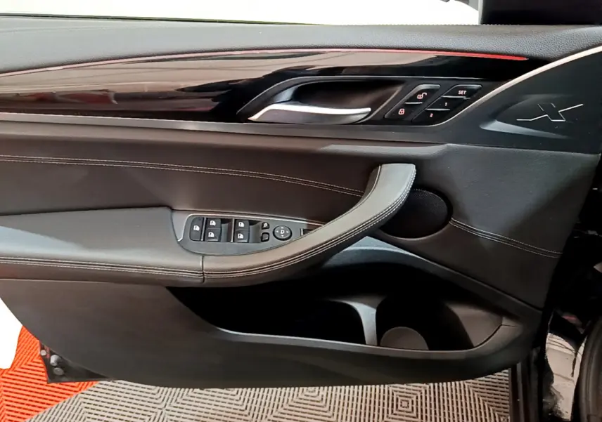 Gros plan sur la porte côté conducteur du BMW X3 noir 2019, avec commandes de vitres et logo X embossé.