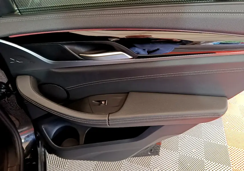 Gros plan sur la porte côté gauche intérieure noire du BMW X3 xDrive20d 2019 avec poignée argentée et coutures blanches.