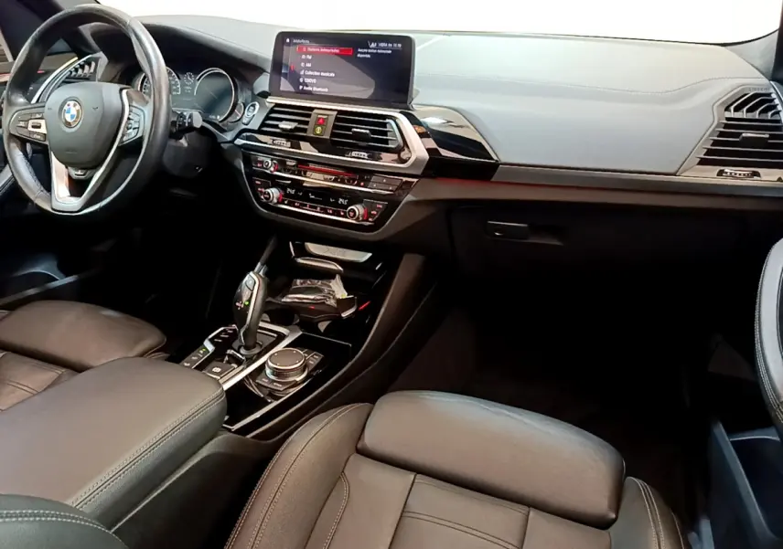 Intérieur BMW X3 xDrive20d 2019 vu côté conducteur, tableau de bord moderne avec écran tactile 10,3 pouces et cuir noir.