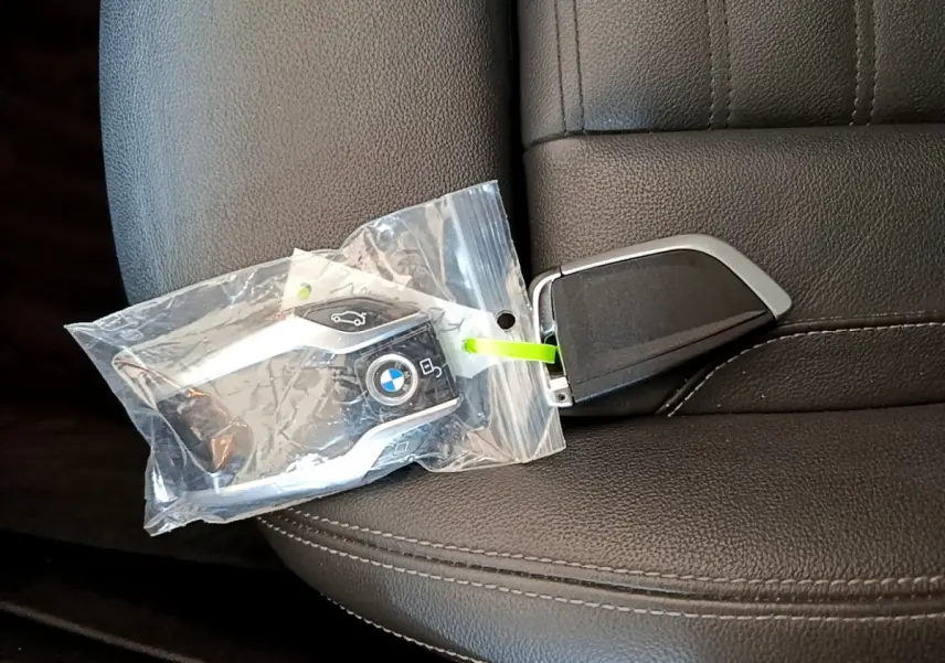 Clé BMW noire avec logo bleu et blanc posée sur un siège en cuir noir à coutures apparentes.