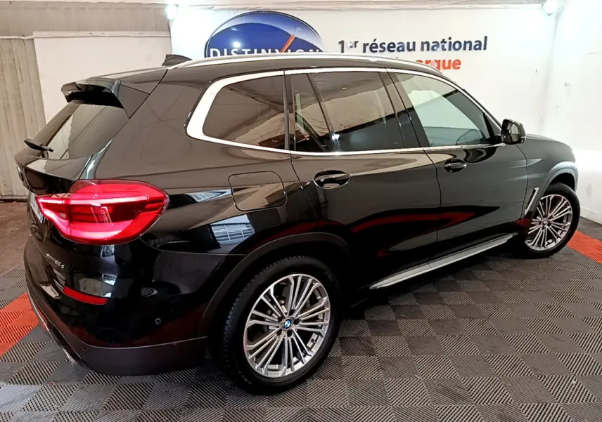BMW X3 xDrive20d noir vu en 3/4 arrière droit, avec jantes alliage et feux arrière LED allumés.