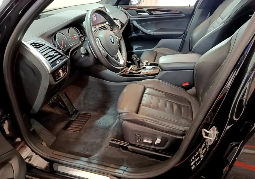 Intérieur noir vu côté conducteur d'une BMW X3 xDrive20d 2019, sièges cuir et tableau de bord moderne.
