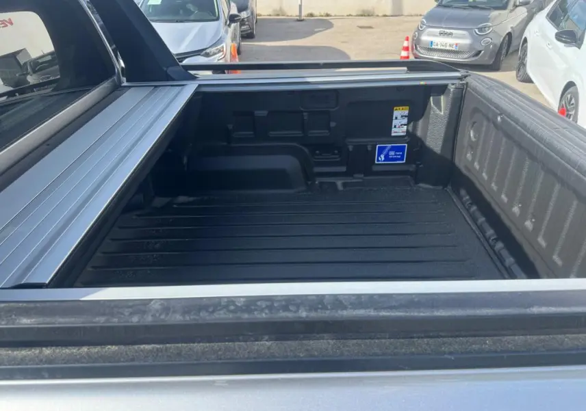 Vue plongeante sur la benne arrière grise du Ford Ranger 2025 avec barres de toit et ridelle ouverte.