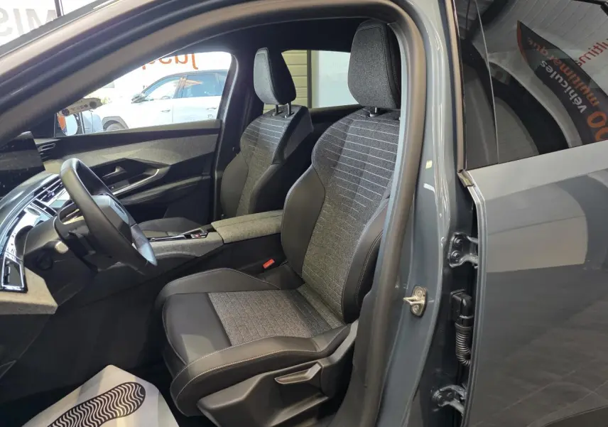 Vue intérieure côté conducteur du Peugeot 3008 hybride 2025 bleu clair, mettant en valeur les sièges tissu et cuir bicolores.