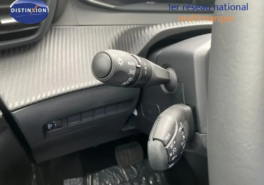 Gros plan sur les commandes au volant d’une Peugeot 208 Hybrid 145ch, avec détails des leviers de réglage et tableau de bord gris.