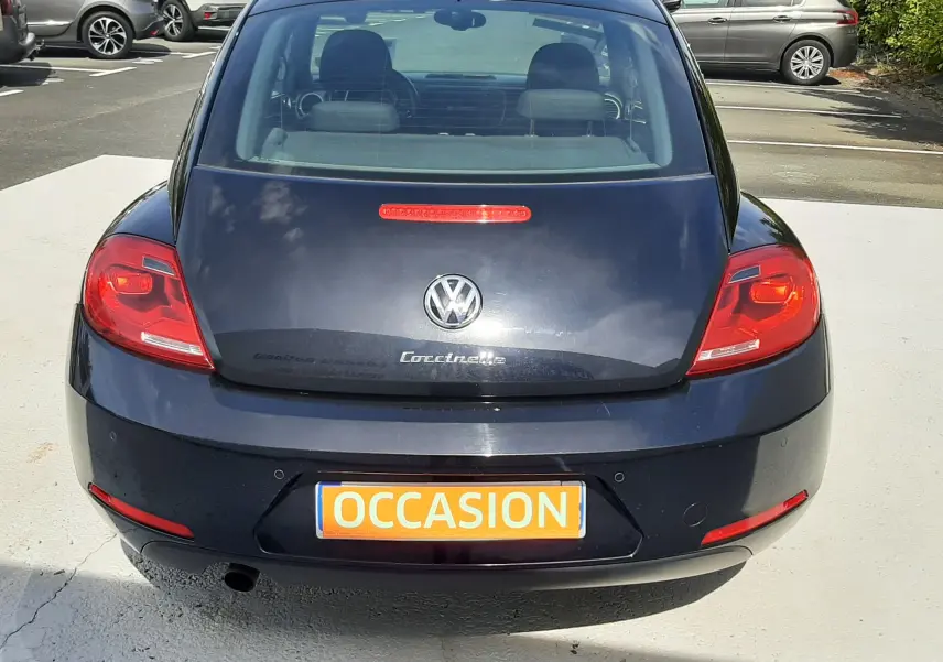 Vue arrière d'une Volkswagen New Beetle noire de 2015 avec plaque "OCCASION" en orange, stationnée en extérieur.