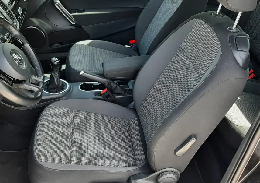 Vue intérieure côté conducteur du Volkswagen New Beetle noir 2015, sièges tissu gris et volant avec levier de vitesse manuel.
