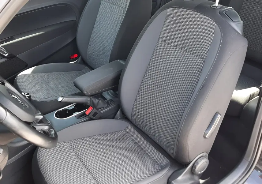 Vue intérieure côté conducteur du Volkswagen New Beetle noir 2015, sièges tissu gris avec accoudoir central.