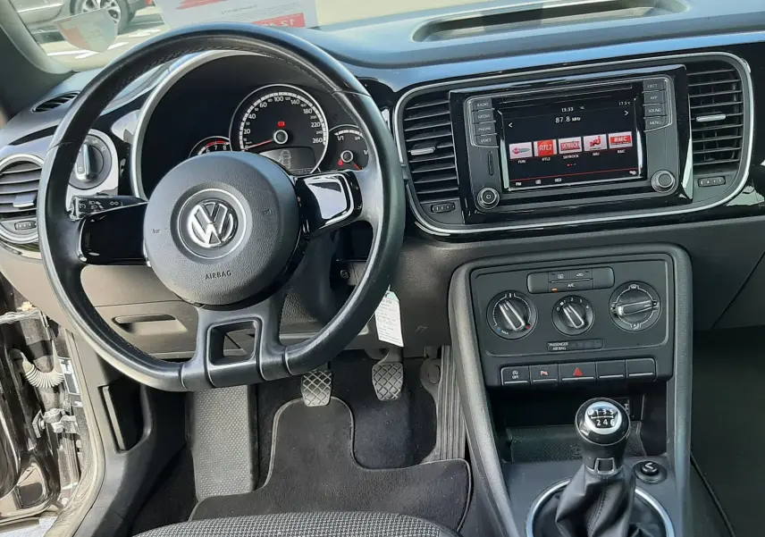 Vue intérieure centrée sur le volant et la console centrale d'une Volkswagen New Beetle noire avec boîte manuelle et écran multimédia.