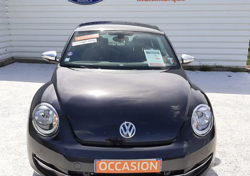 Vue avant d'une Volkswagen New Beetle noire de 2015 avec plaque "OCCASION" et autocollants sur le pare-brise.