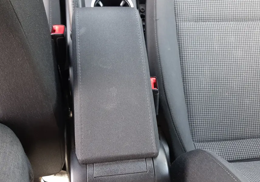 Vue plongeante sur l'accoudoir central noir et les sièges en tissu gris du Volkswagen New Beetle 2015.