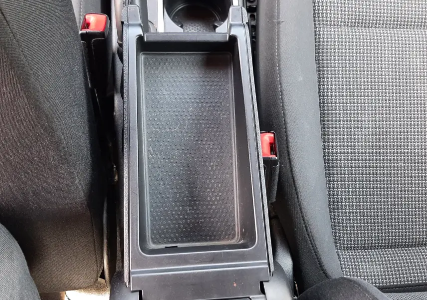Vue plongeante sur la console centrale ouverte du Volkswagen New Beetle noir, montrant porte-gobelet et tissu de siège gris.