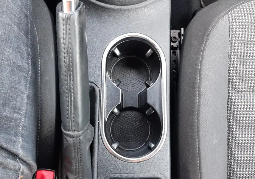 Vue plongeante sur la console centrale noire d’un Volkswagen New Beetle 2015, avec frein à main et porte-gobelets visibles.