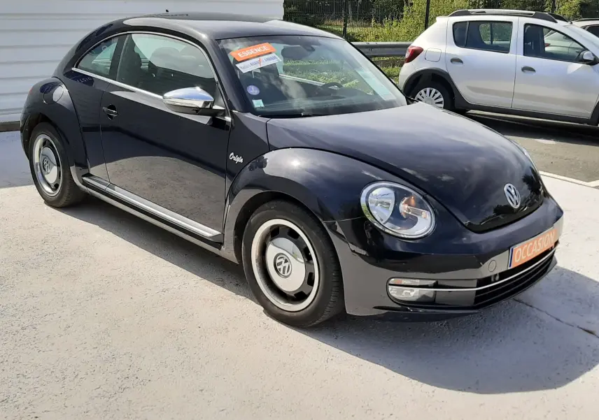 Volkswagen New Beetle noir en 3/4 avant droit, avec jantes originales et badge Origin visible sur l'aile.
