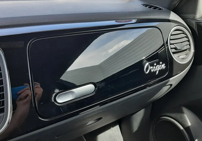 Vue intérieure côté passager du tableau de bord noir brillant du Volkswagen New Beetle 1.2 TSI 105 Origin avec logo "Origin" visible.