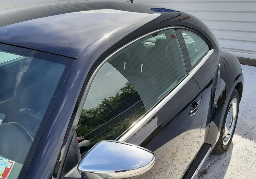 Vue 3/4 avant droit du Volkswagen New Beetle noir brillant, mettant en valeur la forme arrondie et le rétroviseur chromé.