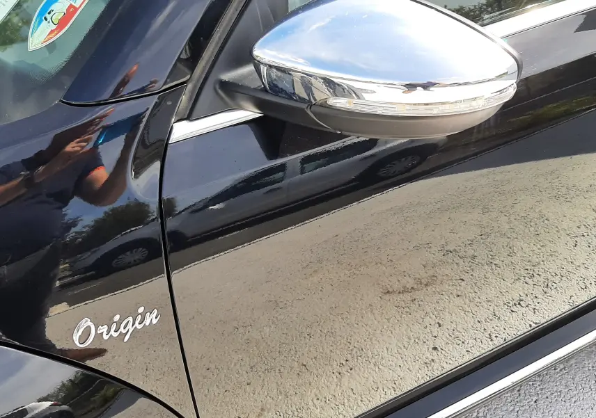 Détail du côté gauche d’un Volkswagen New Beetle noir 2015, avec rétroviseur chromé et logo Origin visible.