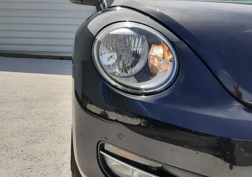 Gros plan sur l'avant gauche du Volkswagen New Beetle noir, mettant en valeur le phare rond et le rétroviseur chromé.