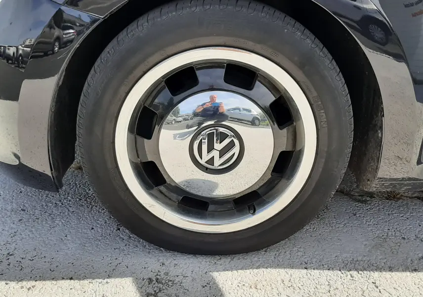 Gros plan sur la roue avant droite noire d’un Volkswagen New Beetle 2015 avec jante chromée et logo VW central.