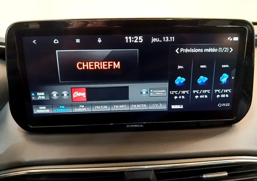 Écran tactile central du Hyundai Santa Fe blanc 2022 affichant la radio Cherie FM et la météo sur tableau de bord.