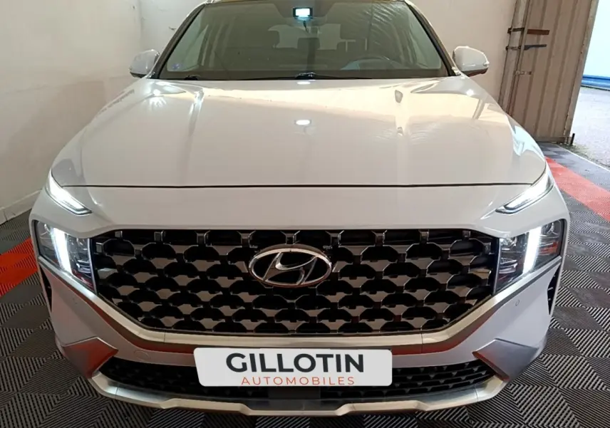 Vue frontale d'un Hyundai Santa Fe blanc avec calandre noire à motifs géométriques et phares LED allumés.