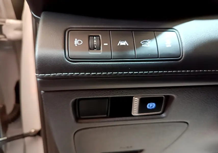 Gros plan sur les commandes de réglage des phares, assistance au maintien de voie et frein de parking électrique du Hyundai Santa Fe blanc 2022.