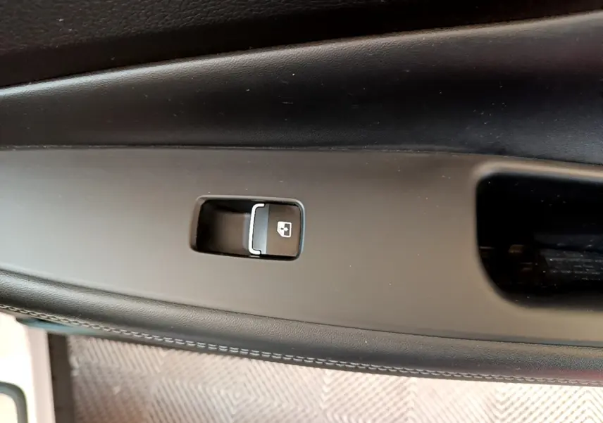 Gros plan sur le bouton de verrouillage des portes intégré dans la garniture noire de la portière intérieure du Hyundai Santa Fe blanc.