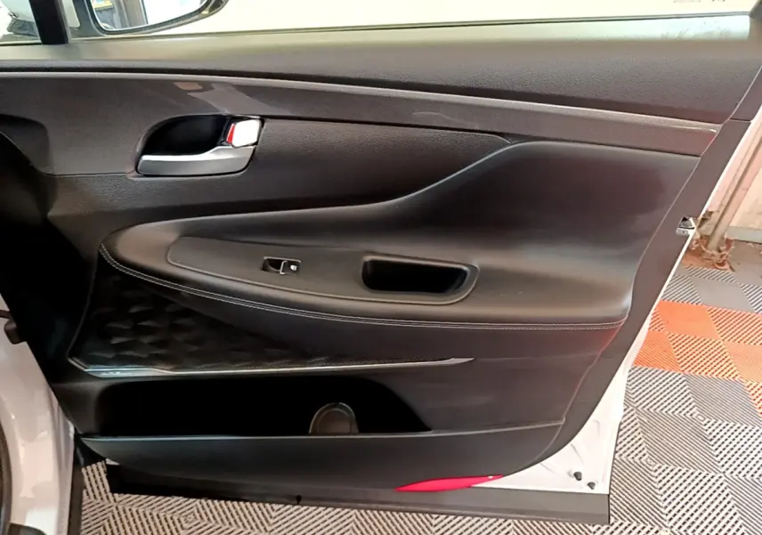 Vue intérieure de la porte avant gauche noire avec poignée chrome du Hyundai Santa Fe blanc 2022.