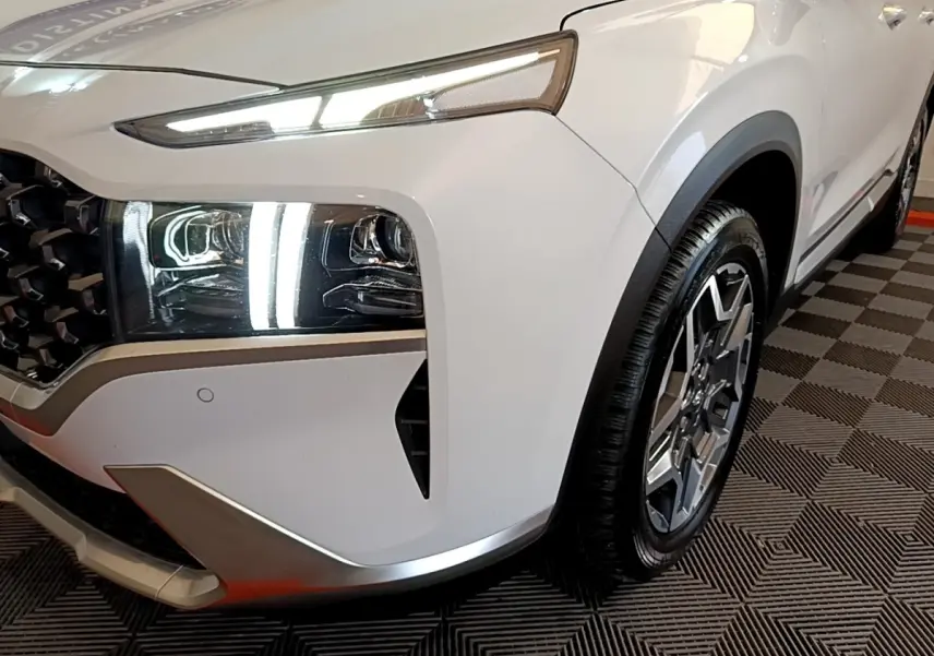 Gros plan sur l'avant droit blanc du Hyundai Santa Fe 2022, mettant en valeur les phares LED et la jante alliage.