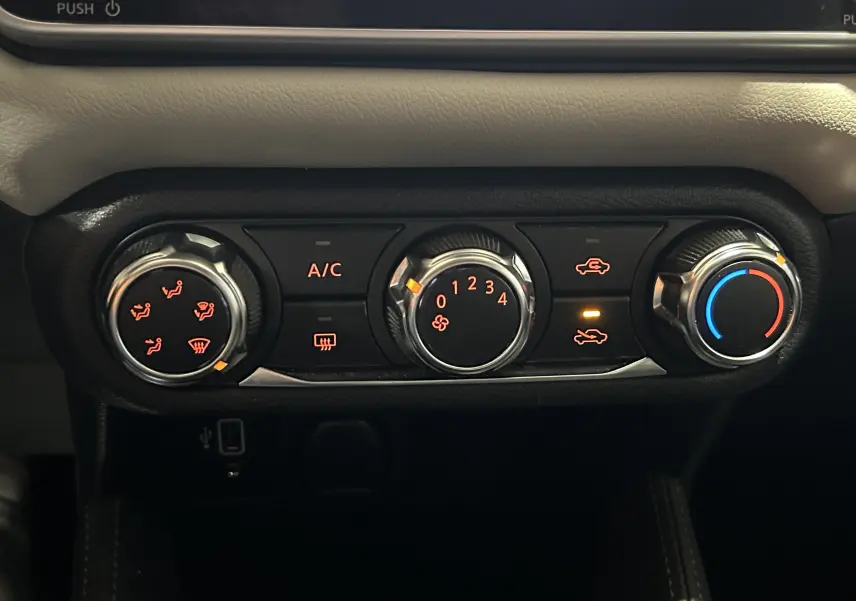 Gros plan sur les commandes de climatisation avec réglages rotatifs et voyants allumés dans une Nissan Micra blanche de 2021.