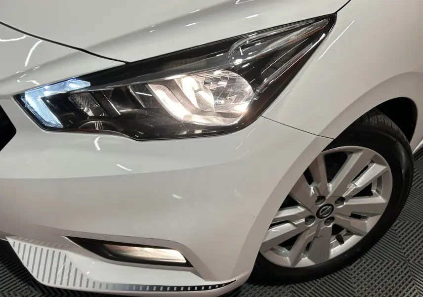 Gros plan sur l'avant droit blanc d'une Nissan Micra 2021, mettant en valeur le phare allumé et la jante alliage.