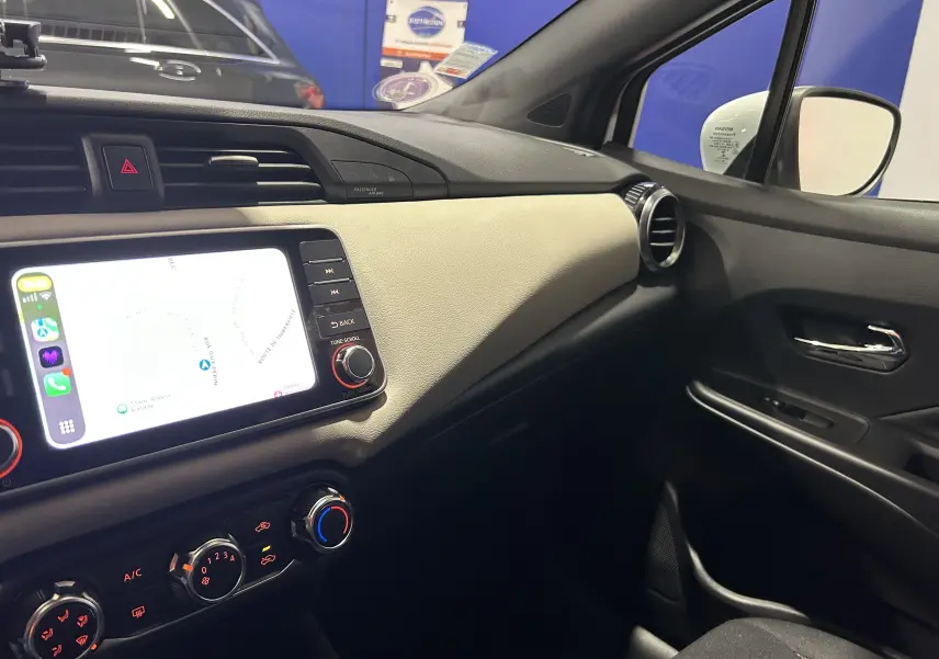 Vue intérieure côté passager de la Nissan Micra blanche 2021 avec écran tactile et commandes de climatisation visibles.