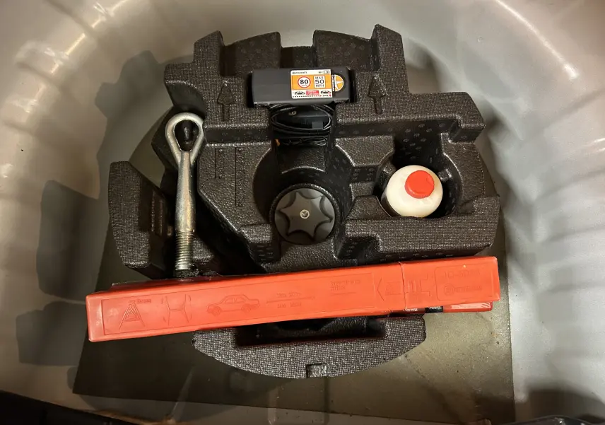 Gros plan sur le rangement d’outils dans le coffre d’une Nissan Micra blanche, avec triangle de signalisation et accessoires.