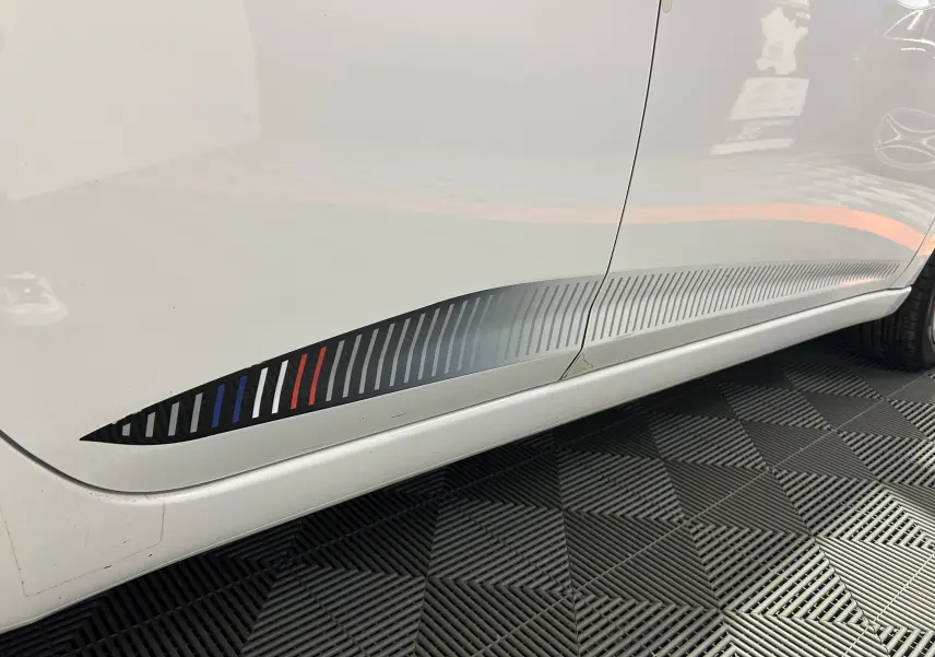 Gros plan sur la partie basse côté gauche d'une Nissan Micra blanche avec un sticker décoratif rayé tricolore.